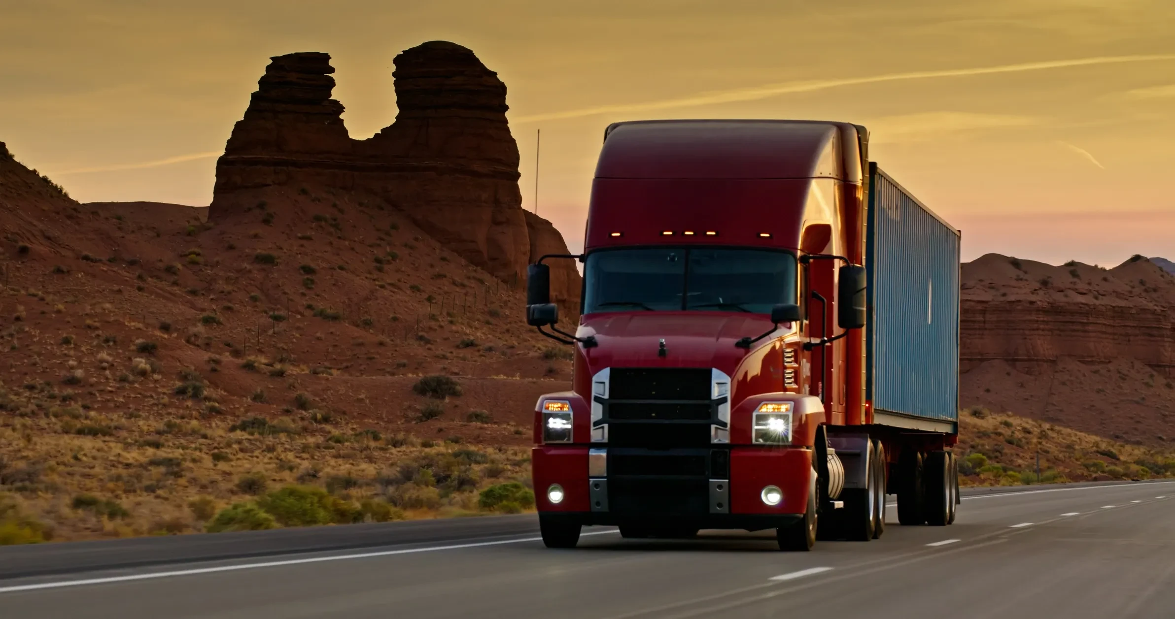 Red semi truck rolling through a desert canyon at golden hour.